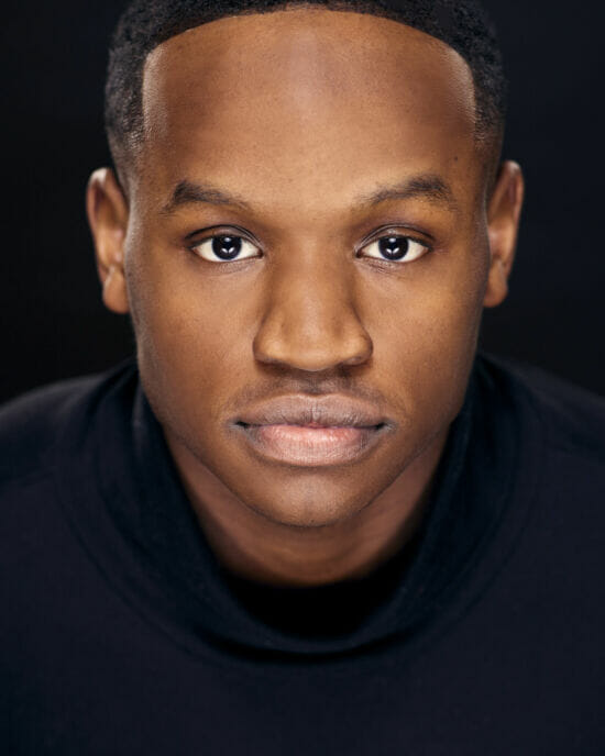 A striking headshot of NYC Actor of Joshua Dawson, wearing black on a black background